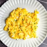 Cottage cheese scrambled eggs with chive sprinkled on top on a plate.