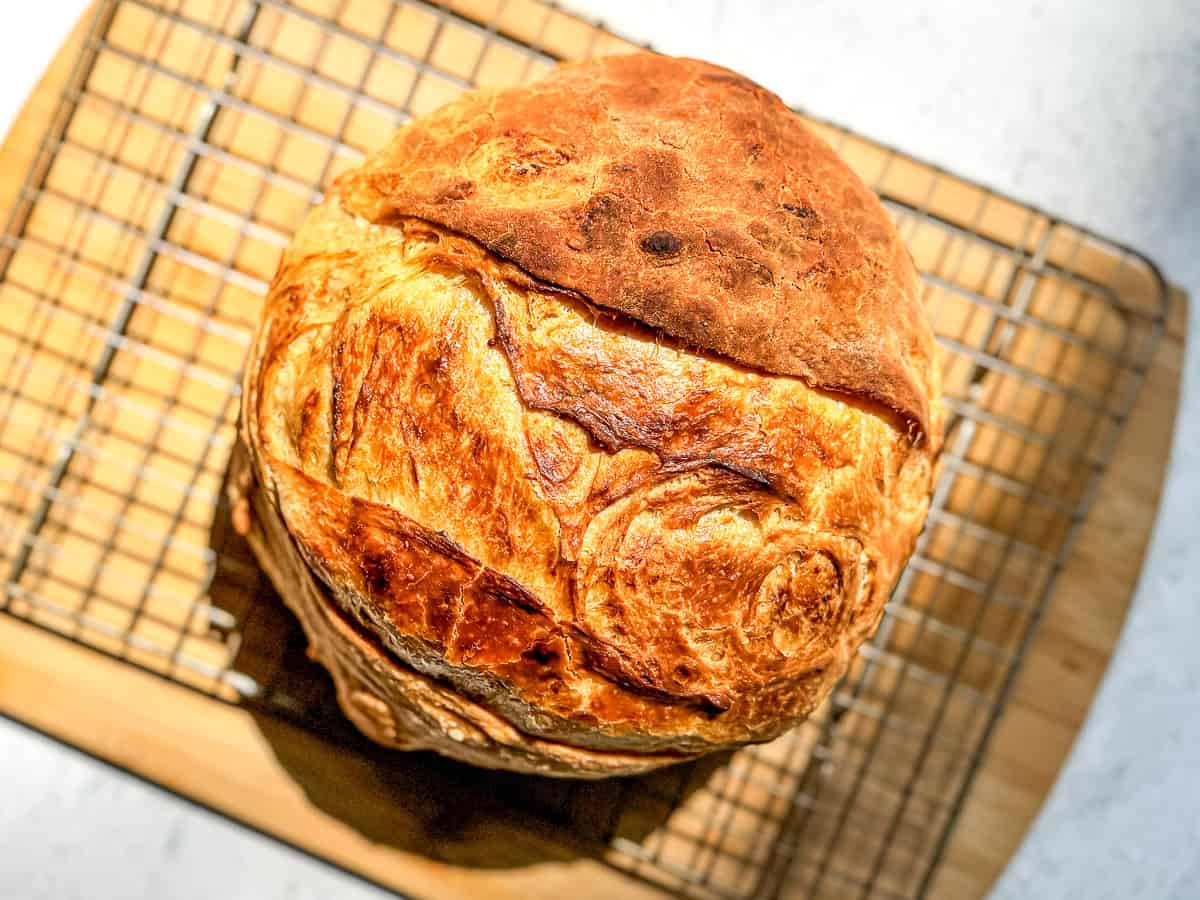 A loaf of croissant bread on a wire rack placed on a wooden cutting board.