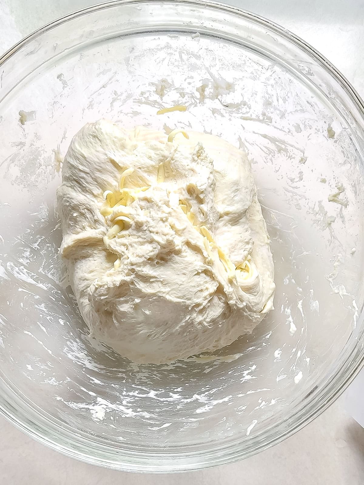 A ball of dough resting in a glass bowl between fold with shreds of butter visible in the seams.