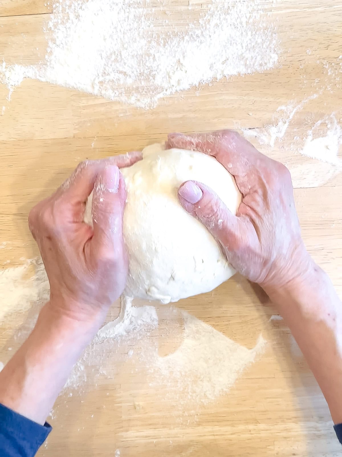 Rolling croissant bread dough into a tight ball on a floured counter.