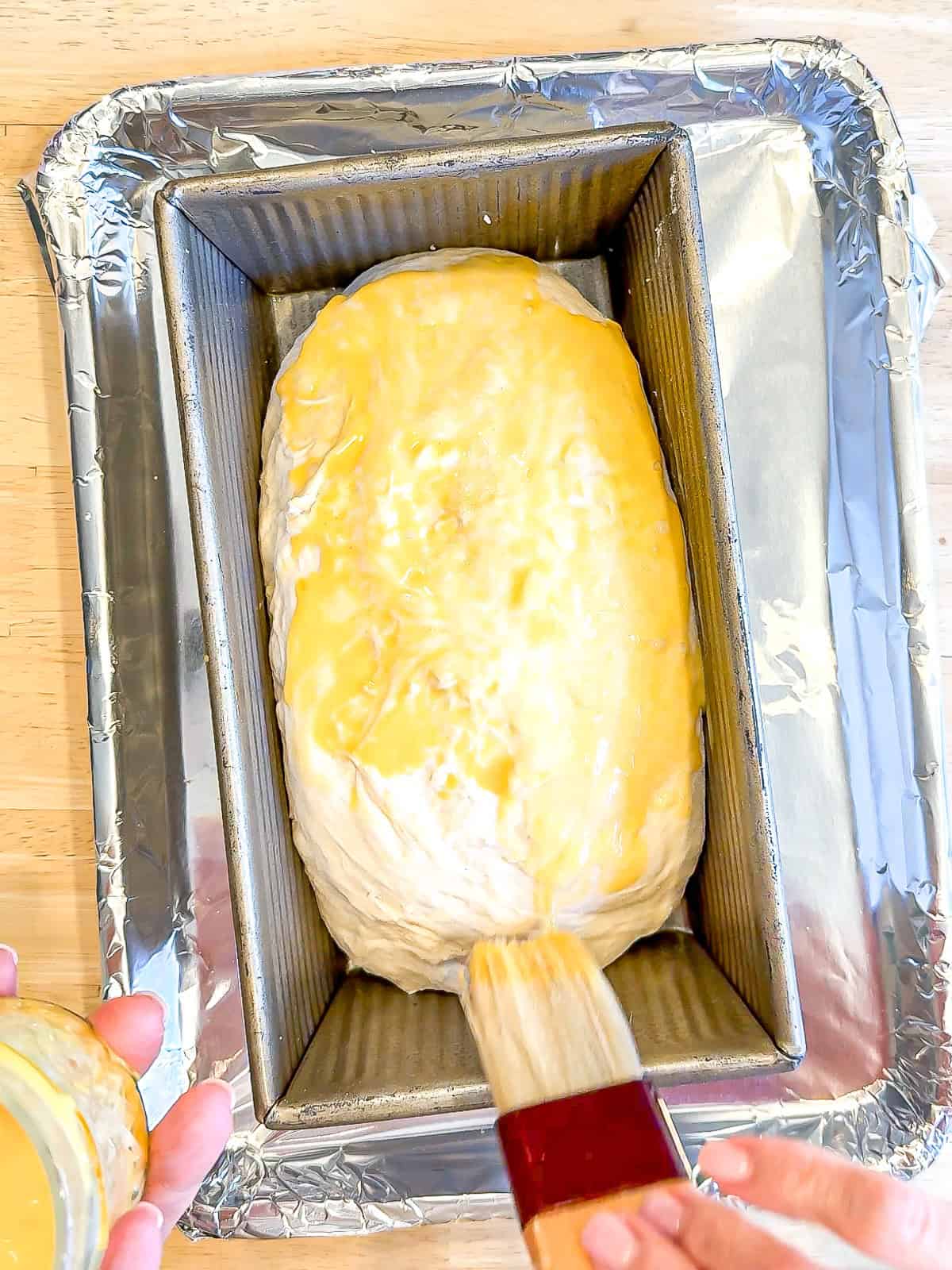 Brushing a croissant loaf with an egg wash.