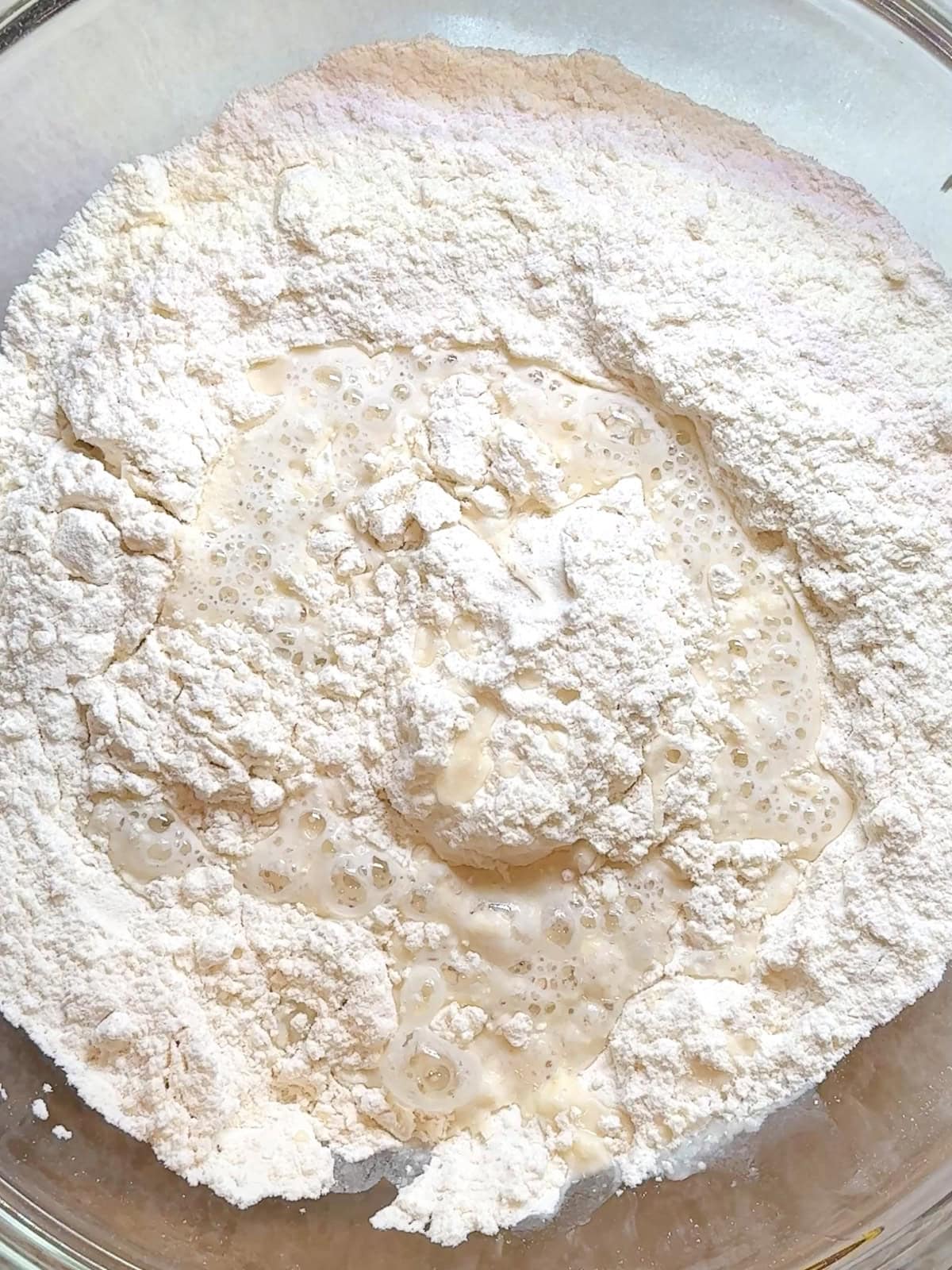 Butter infused flour mixture with yeast and water added to it just before mixing in a glass bowl.
