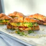 Side view of croissant breakfast sandwiches on a parchment paper lined sheet pan.