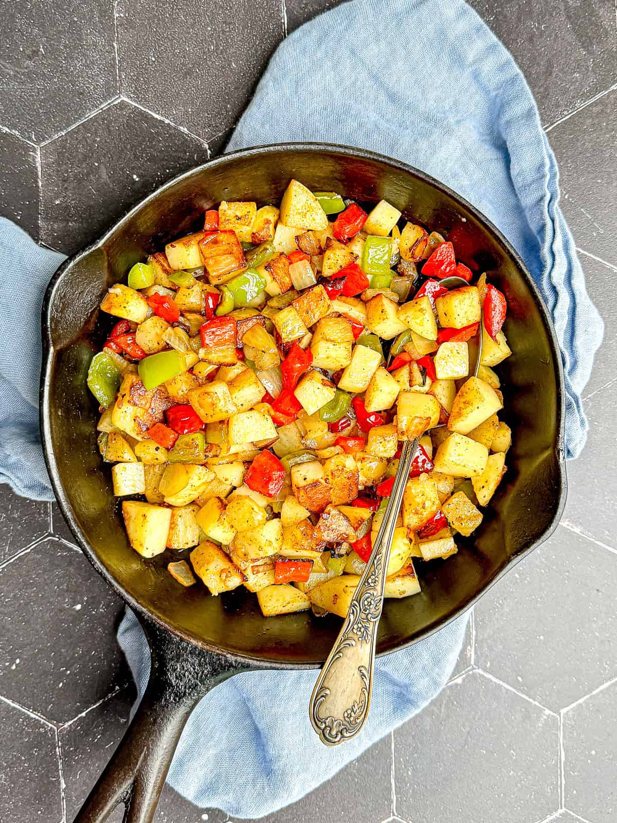 Potatoes O'Brien in a cast-iron pan with an antique spoon.