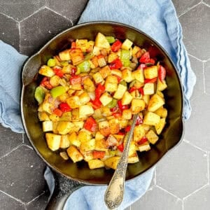 Potatoes O'Brien in a cast-iron pan with an antique spoon.