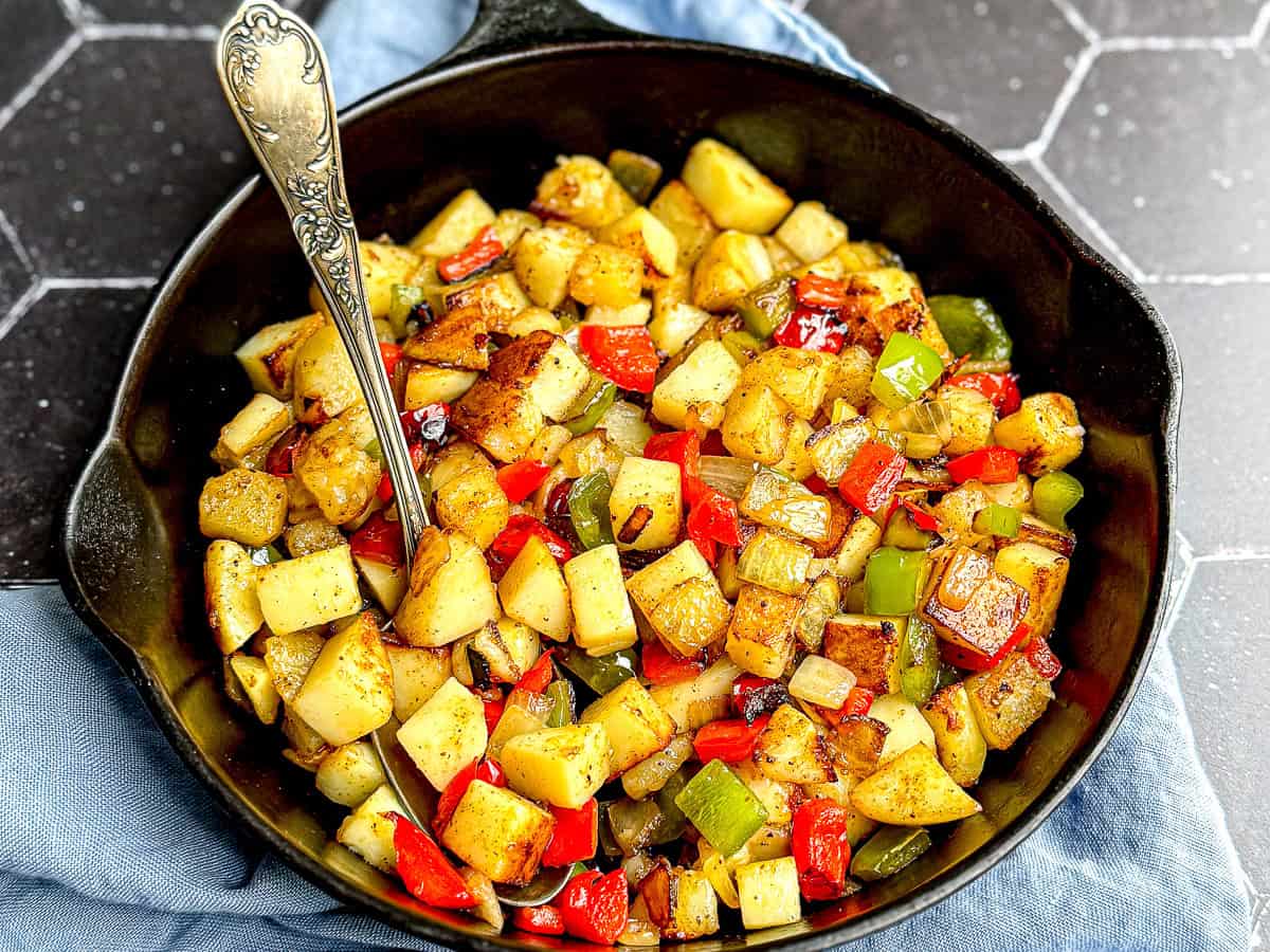 Potatoes O'Brien in a cast-iron pan with an antique spoon.