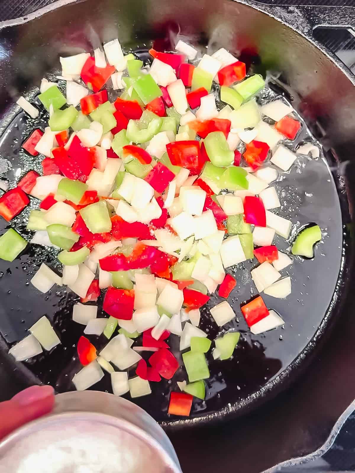 Sautéing red and green bell peppers and onions all diced in a cast-iron pan.