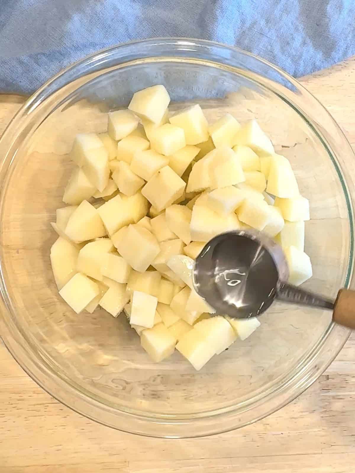 Adding water to diced potatoes in a glass bowl before microwaving for five minutes.
