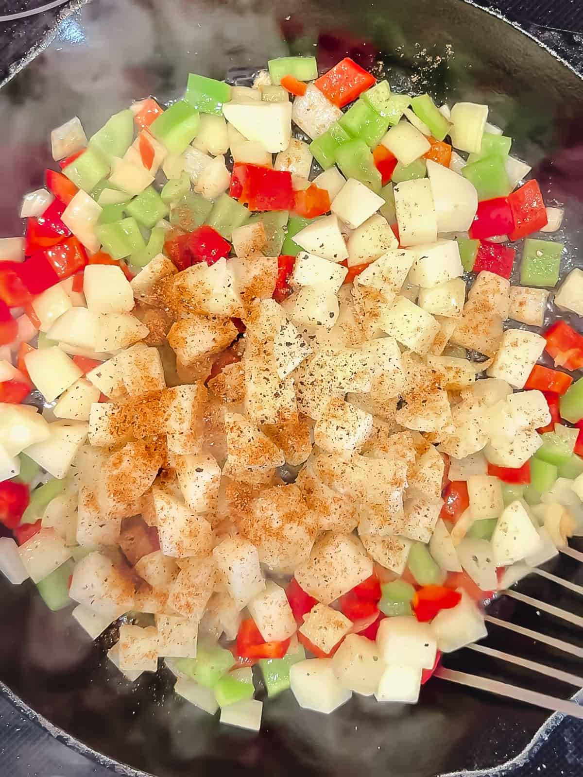 Sautéed vegetables, par cooked potatoes, and seasonings, in a cast-iron pan.