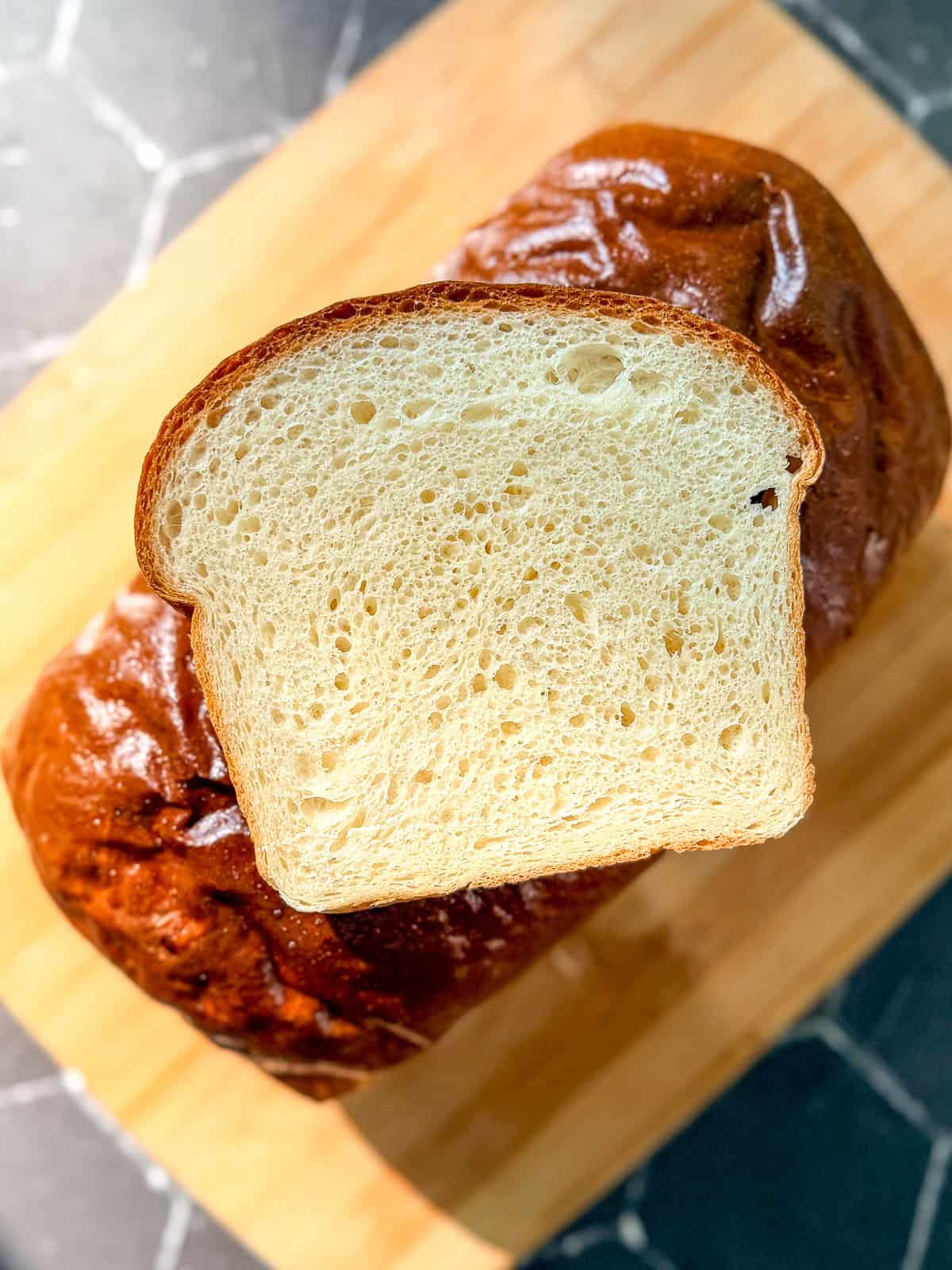 A slice of white bread sitting on top of a loaf of bread.