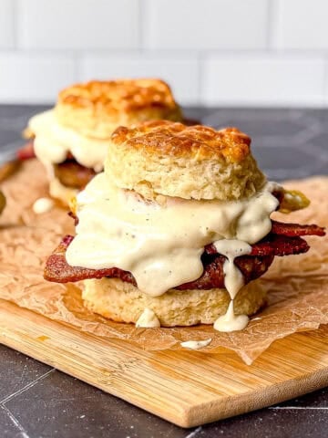 Two breakfast burgers with gravy on a parchment paper covered wooden cutting board.