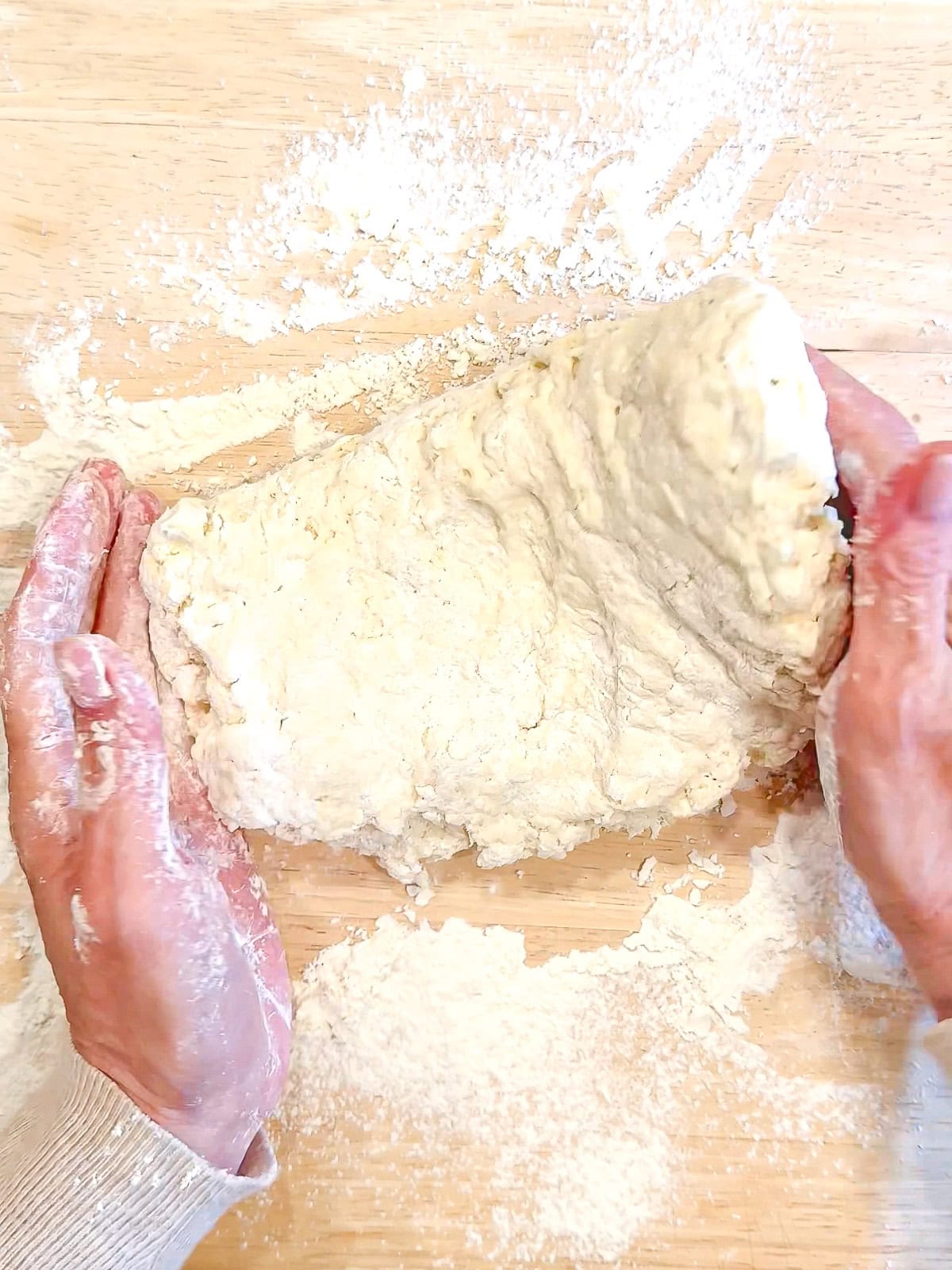 Gently folding biscuit dough over onto itself on a wooden counter.
