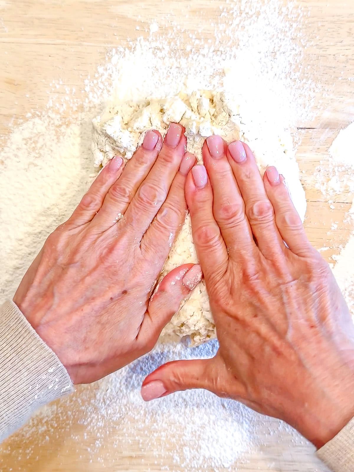 Gently bringing biscuit dough together on a wooden counter.