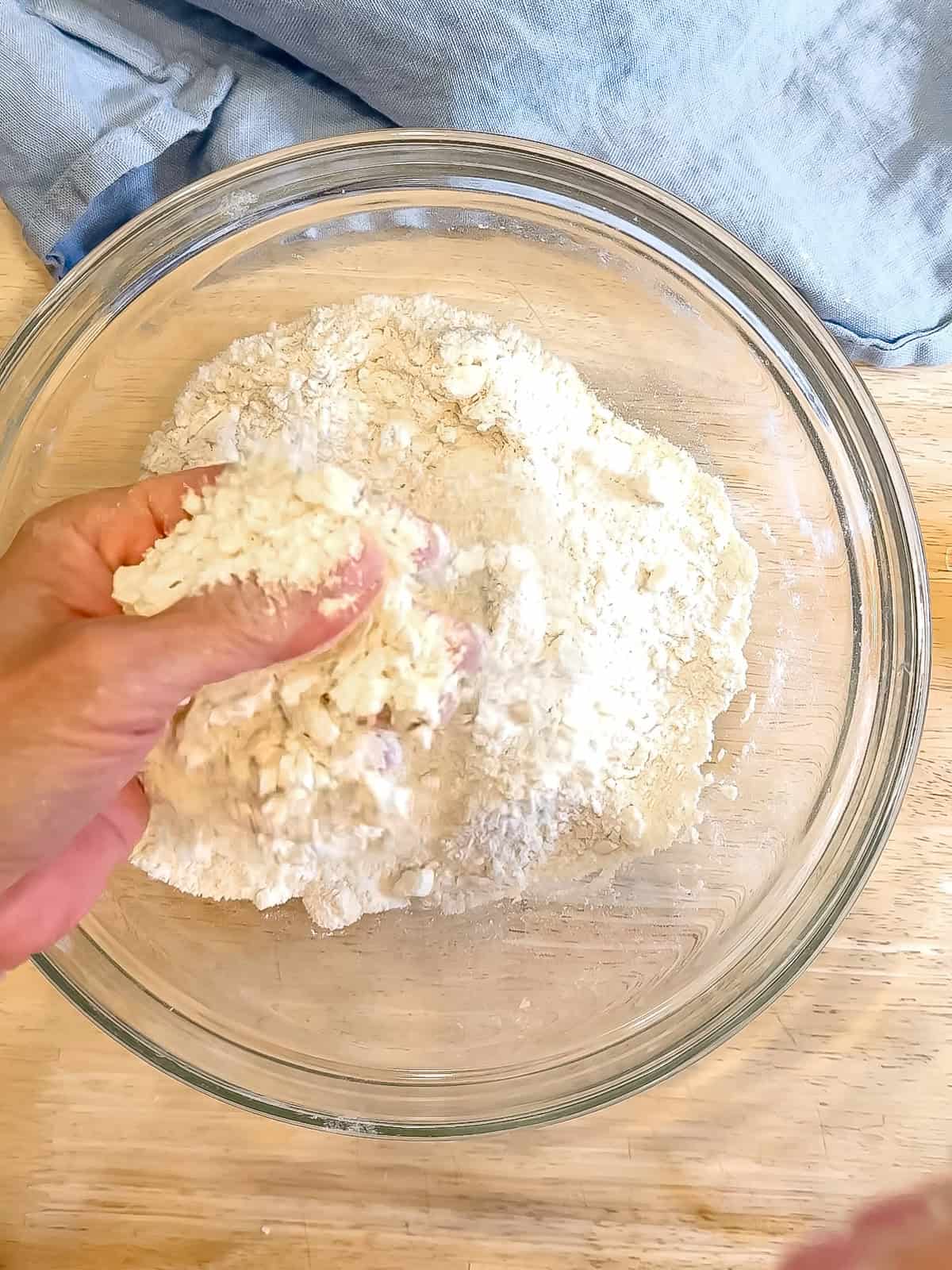 Author's hand holding flour and butter mixture in a glass bowl.