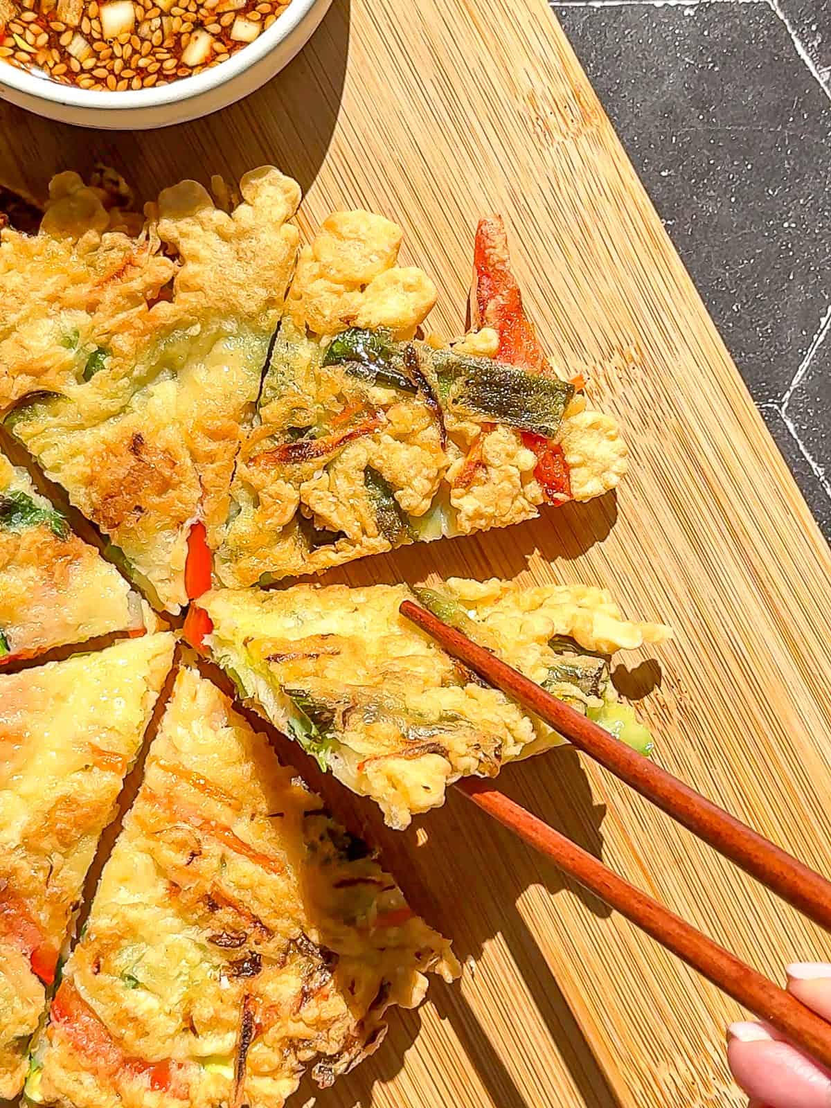 Picking up a cooked Korean vegetable pancake with chopsticks.