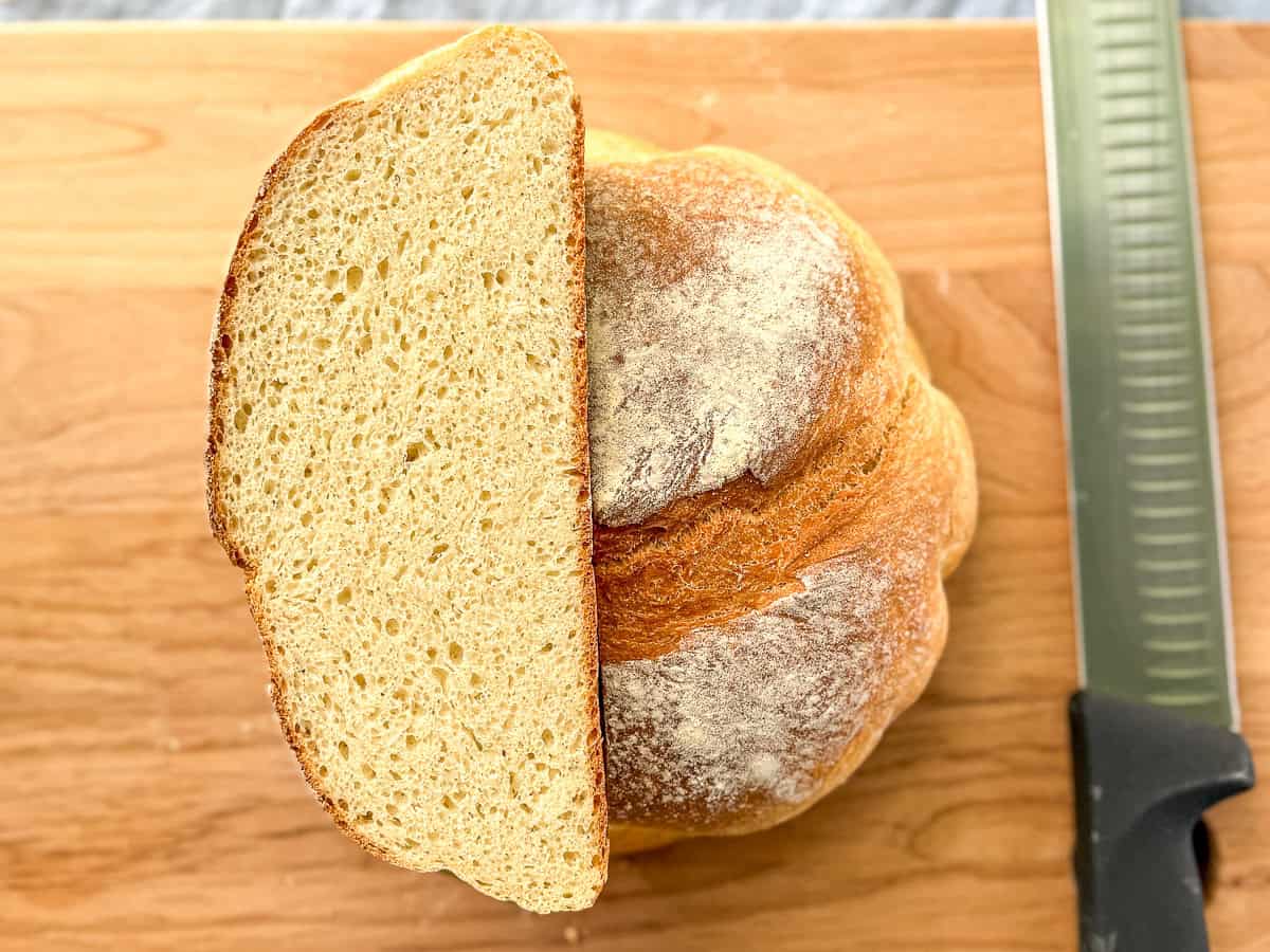 Artisan loaf of bread on a wooden cutting board next to a knife.