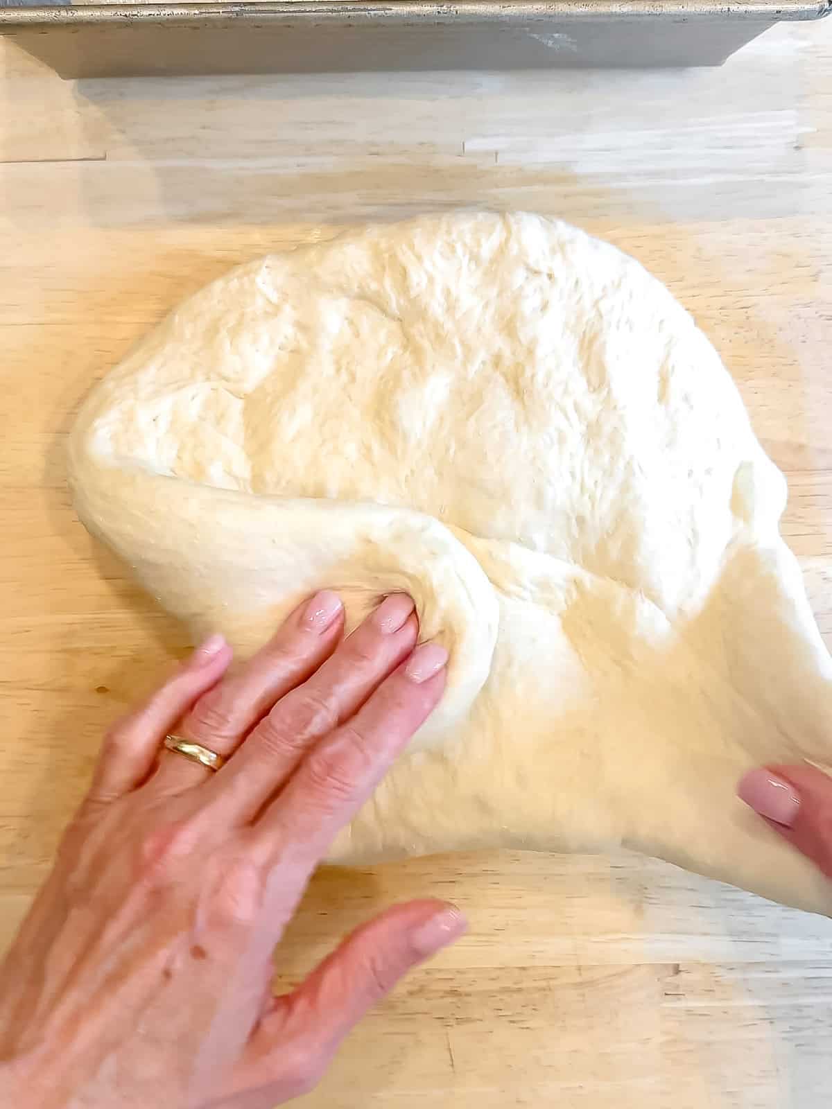 Shaping a loaf of bread on a wooden counter.