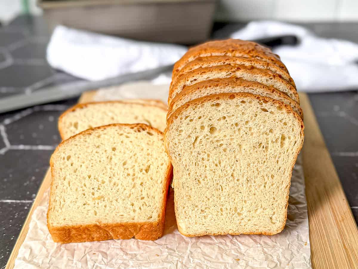 A sliced loaf of one hour bread on a wooden cutting board sitting on a black counter.