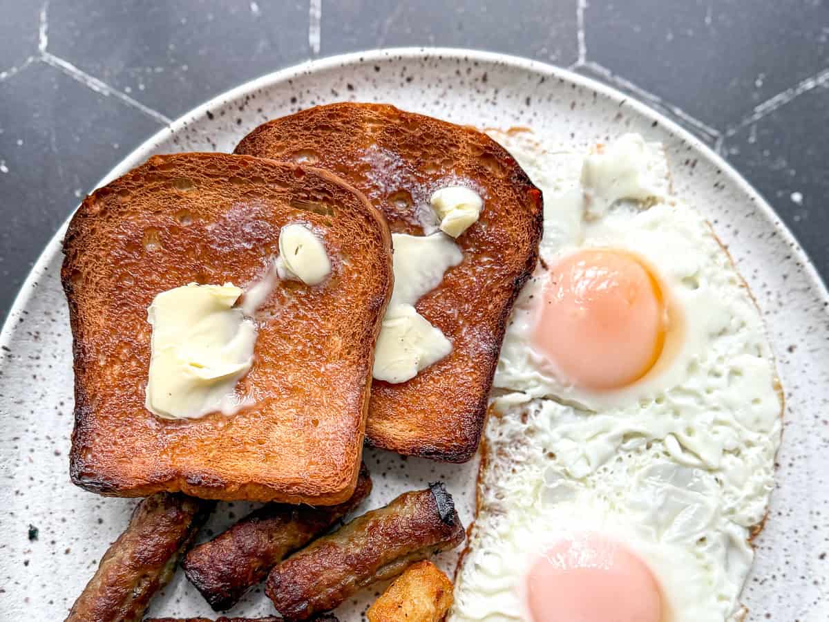 Toasted one hour bread with sausage and eggs on a white plate.