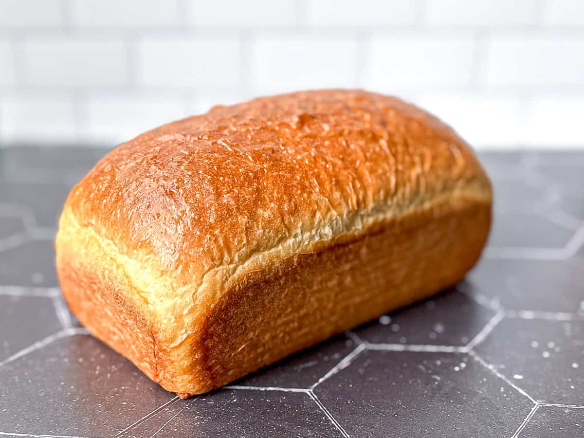 A loaf of bread on a black counter against a white tile backdrop.