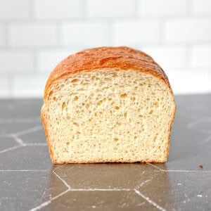 View of a loaf of bread on a black counter against a white tile backdrop.