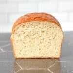 View of a loaf of bread on a black counter against a white tile backdrop.