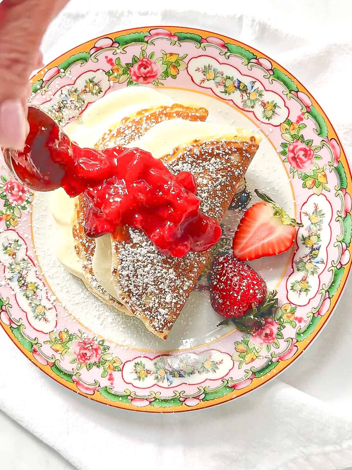 Drizzling strawberry sauce on top of cheesecake filled pancakes.