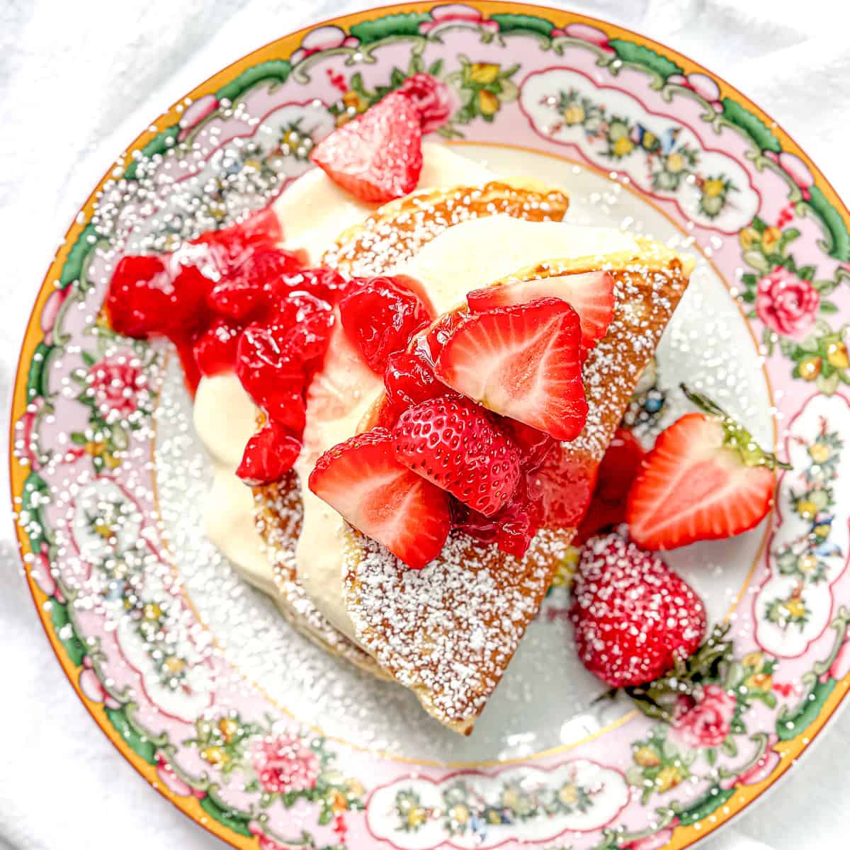 Top view of cheesecake filled pancakes topped with strawberry sauce and fresh strawberries.