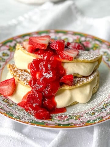 Side view of cheesecake filled pancakes topped with strawberry sauce and fresh strawberries.
