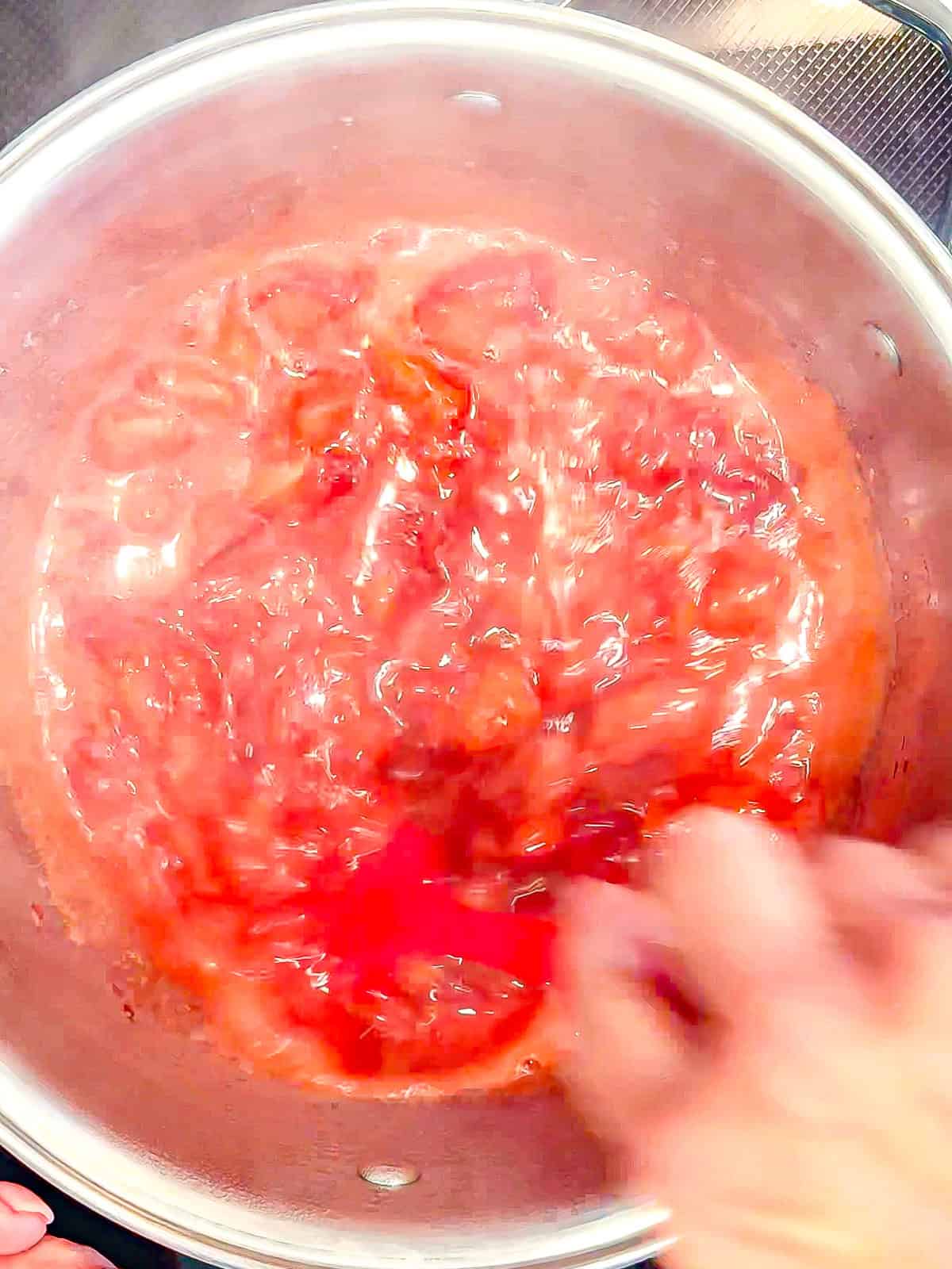 Simmering strawberry sauce in a small saucepan.