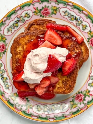 French toast with strawberries and strawberry cream on a floral plate.