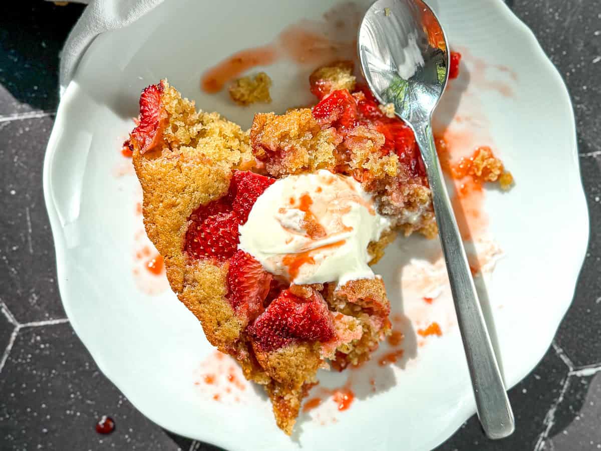 Strawberry cake on a white plate with a silver spoon.