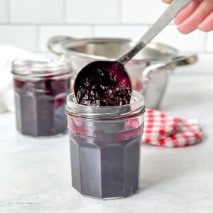 Ladling cooked blueberry jam into a small glass jar.