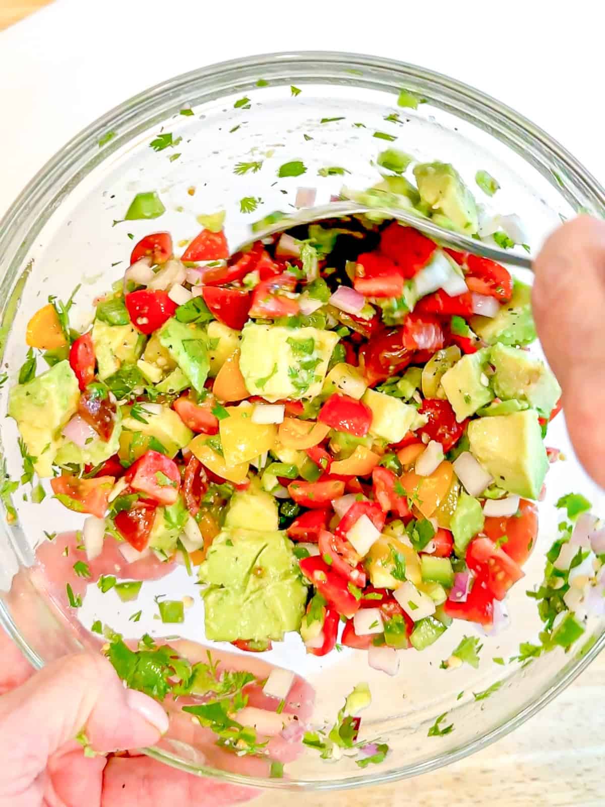 Mixing avocado pico de gallo in a glass bowl.