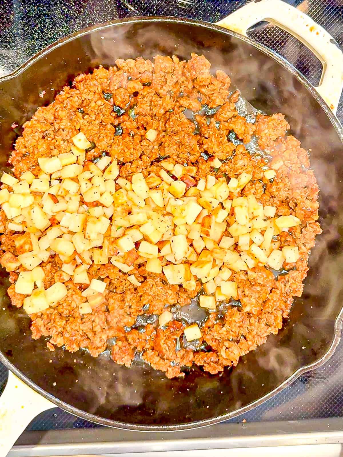 Adding potatoes to chorizo in a cast-iron pan.