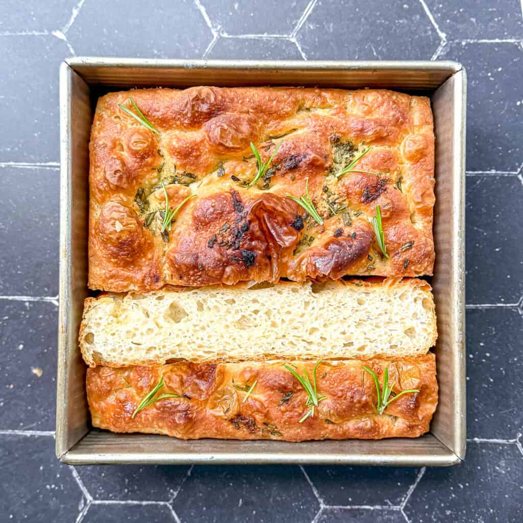 Focaccia in a square pan on a black background.