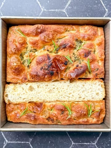 Focaccia in a square pan on a black background.