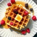 Mochi waffle with fruit, butter, and syrup, on a beige plate.