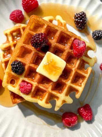 Mochi waffle with fruit, butter, and syrup, on a beige plate.
