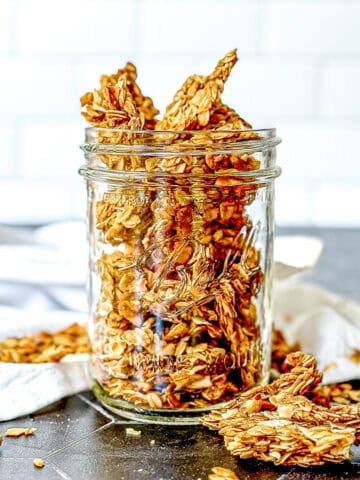 Stove top granola in a mason jar on a black background with a white napkin nearby.