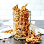 Stove top granola in a mason jar on a black background with a white napkin nearby.