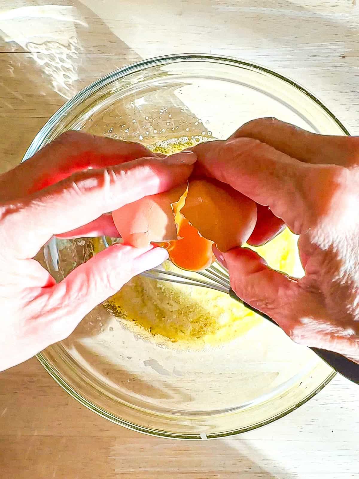 Cracking an egg into ingredients in a glass bowl.