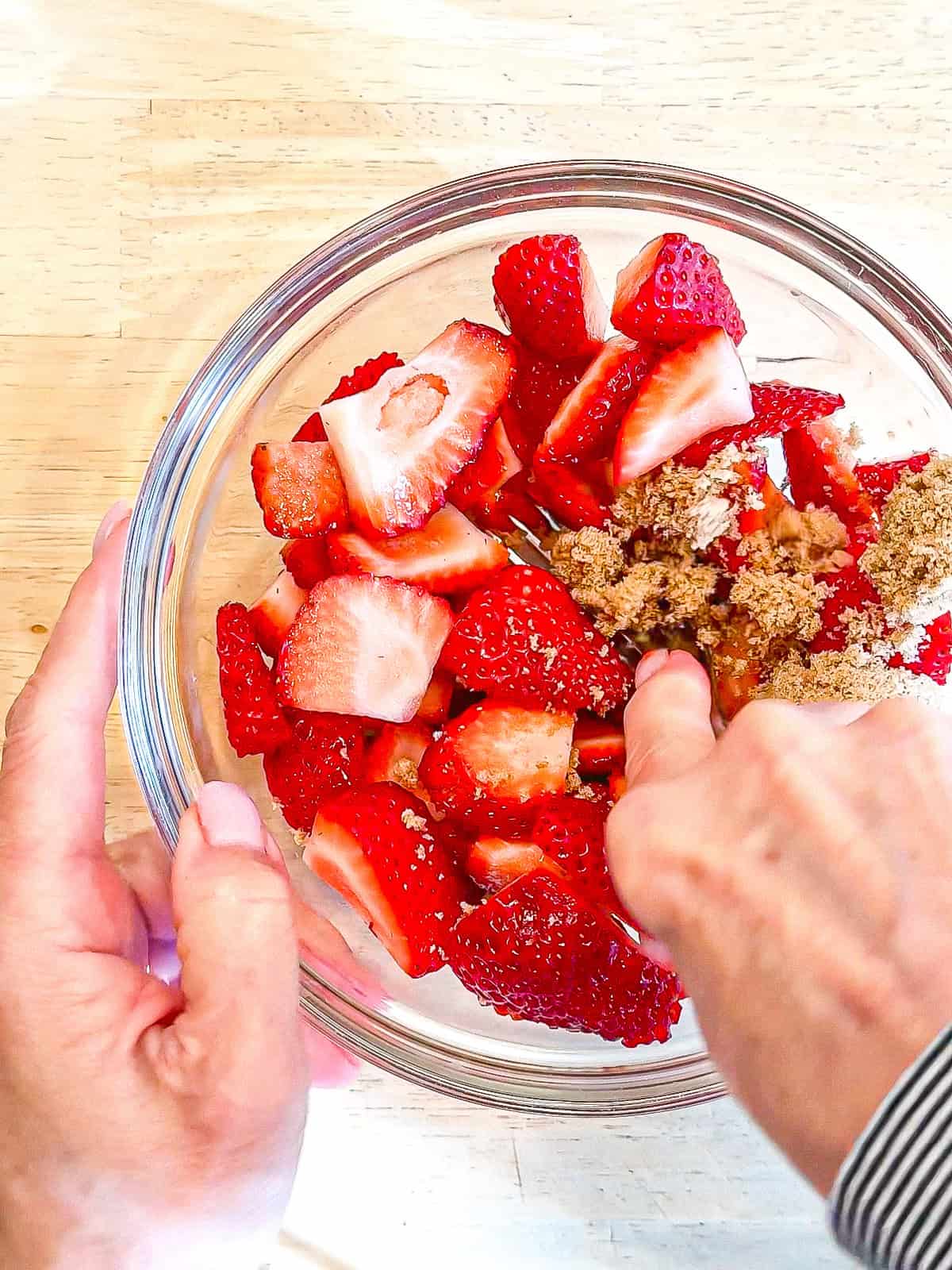 Mashing strawberries and a brown sugar and a glass bowl.