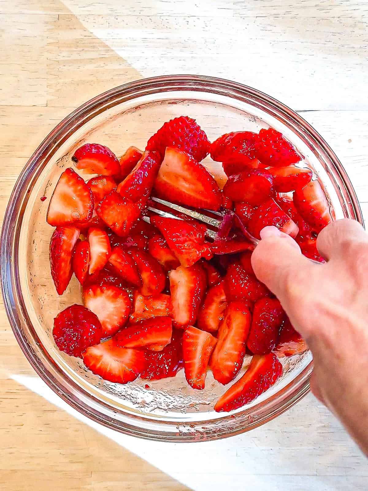 Mashing strawberries with a fork and a glass bowl.