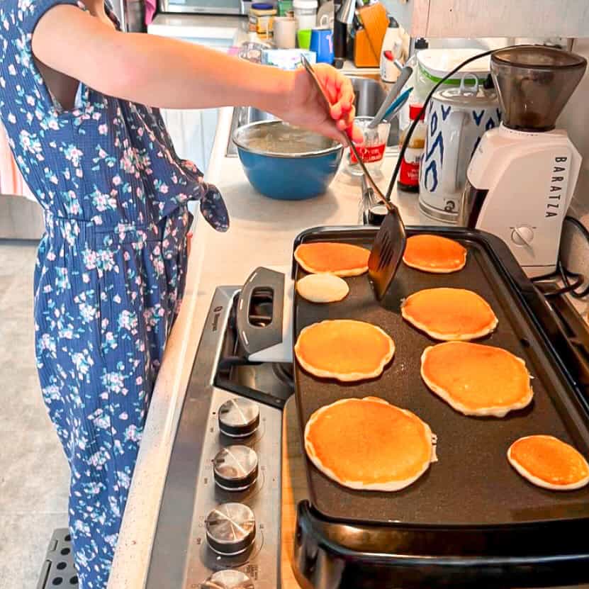 Child making pancakes on a griddle.