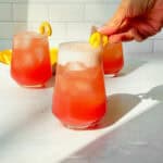 A hand adding garnish to a drink in a glass.
