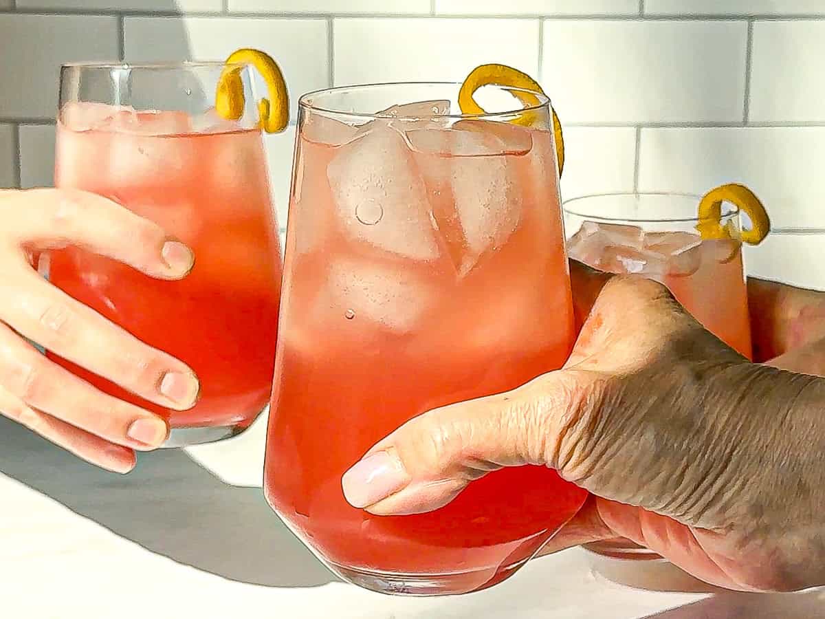 Two people holding glasses of aperol spritz with orange zest curls.