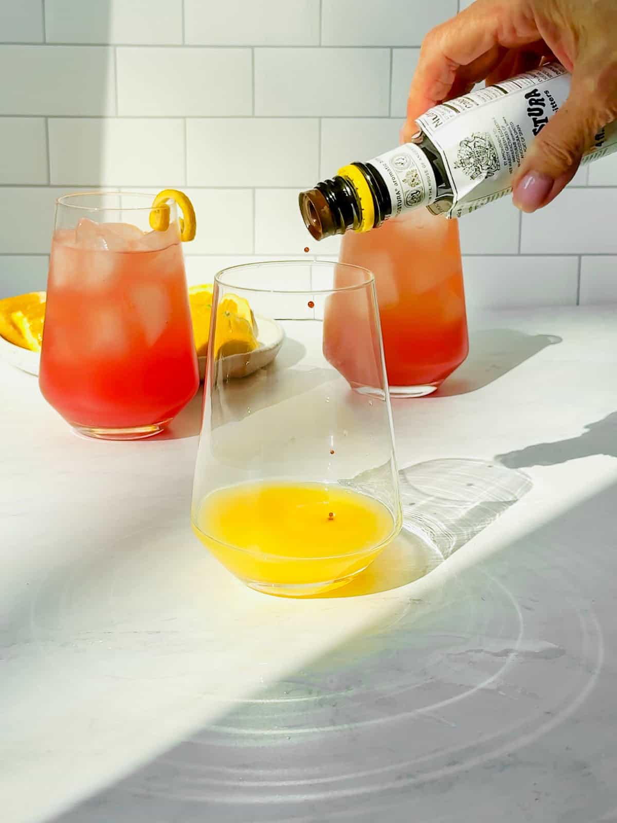 A person pouring bitters into a drink in a glass.