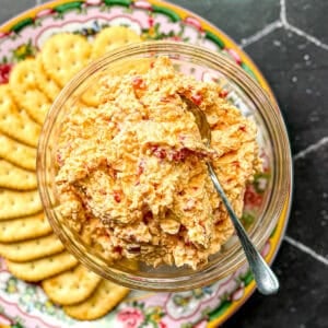 Pimento cheese in a glass bowl on a plate with crackers.