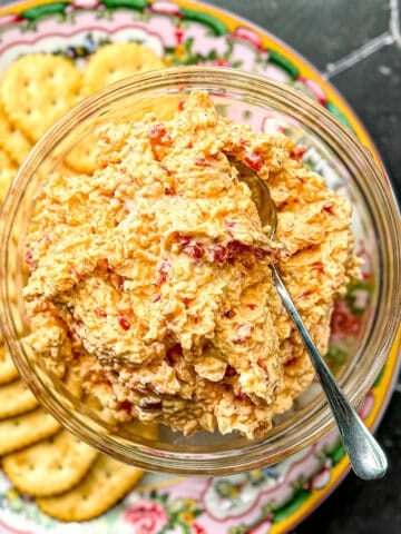 Pimento cheese in a glass bowl on a plate with crackers.